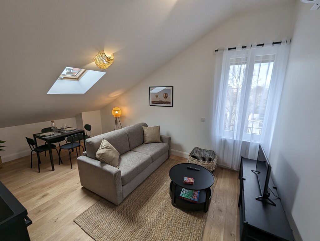 Salon et salle à manger pour un airbnb comprenant une table pour quatre personnes, un canapé lit deux places et un espace TV.