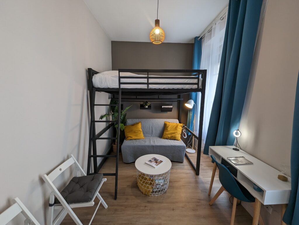 Studio étudiant avec un lit en mezzanine et un petit canapé convertible d'appoint. Le thème est gris, jaune et bleu.